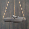 The Earthy Anthracite Bamboo Hanging Bird Bath/Feeder W23.3cm is a gray, frost-proof ceramic feeder with a bird figurine in the center, suspended by ropes against dark wood.