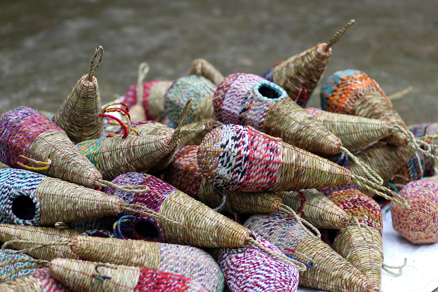 A collection of Wildlife World Tahera Artisan Wild Bird Nesters, designed in an elegant fair trade teardrop shape with small circular openings. These nesters are made from natural fibers and adorned with various colorful patterns, showcasing their handcrafted quality as they rest on a stone surface.