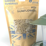 A 450g "Premium Sunflower Hearts" package from etree, featuring a brown compostable bag with blue sun and British flag designs, is next to a green bird feeder.
