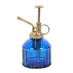 The Small Blue Glass Plant Mister features a gold metal pump and nozzle, ideal for indoor garden enthusiasts. Its cylinder-shaped bottle has a textured surface and a small handle for easy use, adding a charming vintage feel to any space.