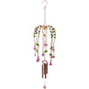 The Fuchsia Windchime, a decorative, hand-crafted piece adorned with pink and purple flower ornaments and green leaf accents, elegantly hangs from a hook. Several metal rods and a pendant beneath the flowers form the chiming element. This delicate and colorful design is perfect for both indoor and outdoor display.