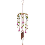 The Fuchsia Windchime, a decorative, hand-crafted piece adorned with pink and purple flower ornaments and green leaf accents, elegantly hangs from a hook. Several metal rods and a pendant beneath the flowers form the chiming element. This delicate and colorful design is perfect for both indoor and outdoor display.
