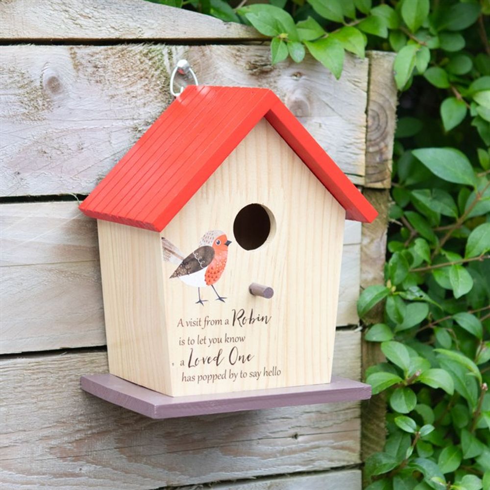 The Garden Robin Bamboo Bird House, with a red roof and painted robin design, hangs on a wooden wall amid greenery. It features the text: "A visit from a Robin is to let you know a Loved One has popped by to say hello," making it an ideal garden accessory for added charm.
