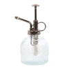 The Small Patterned Glass Plant Mister features a vintage design with a metallic pump and nozzle. This ornate bottle, ideal for indoor gardens, has an embossed pattern and a handy side finger loop for easy handling.