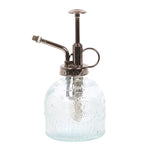 The Small Patterned Glass Plant Mister features a vintage design with a metallic pump and nozzle. This ornate bottle, ideal for indoor gardens, has an embossed pattern and a handy side finger loop for easy handling.