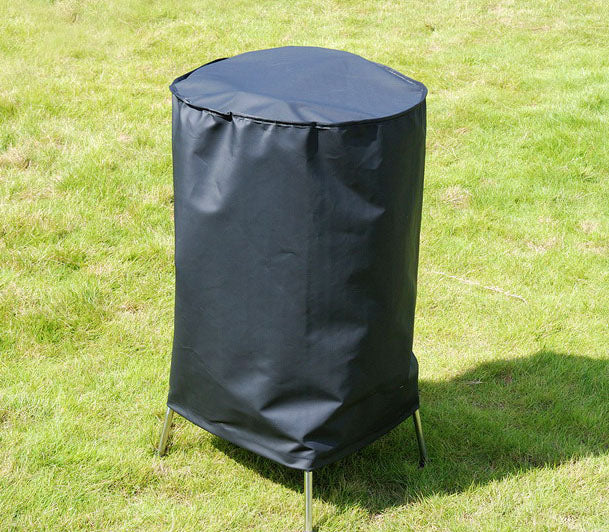 A tall, black cylindrical Premium Kettle Barbecue Cover stands on a grassy lawn with metal legs. Designed for outdoor furniture, this UV-protected PVC marvel offers waterproof protection, ensuring lasting durability against the elements. Dimensions: 71(Dia.) X 90(H) cm.