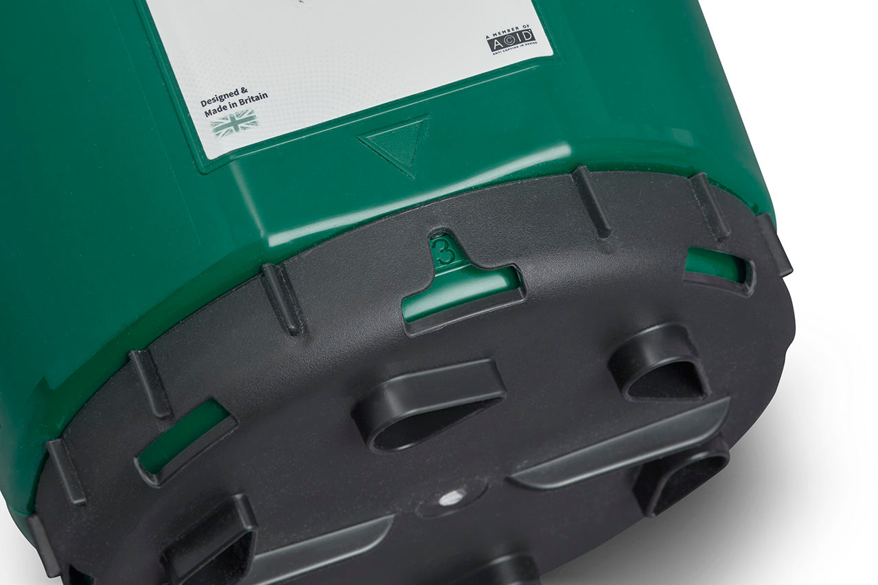 Close-up view of the bottom part of a green and black Multipurpose Garden Spreader with Twist & Shake Action. "Designed & Made in Britain" is visible on a label at the top, alongside a British flag. The base features several openings and extrusions, indicating an adjustable flow rate suitable for multiple uses.