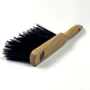 A wooden-handled brush with hard black bristles, laid flat on a white background. The handle, branded as the Hand Brush with Hard Bristles, has a hole near the end for hanging and features a decorative clover design etched into the wood.
