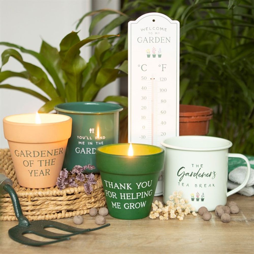 A cozy garden-themed setup includes the "Thank You for Helping Me Grow" citronella candle, a ceramic plant pot, thermometer, garden trowel, and a mug labeled "The Gardener's Tea Break," creating a serene outdoor space.