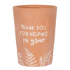 The Thank You For Helping Me Grow Terracotta Plant Pot features white text saying "Thank you for helping me grow" and charming white leaf and plant illustrations along the bottom.