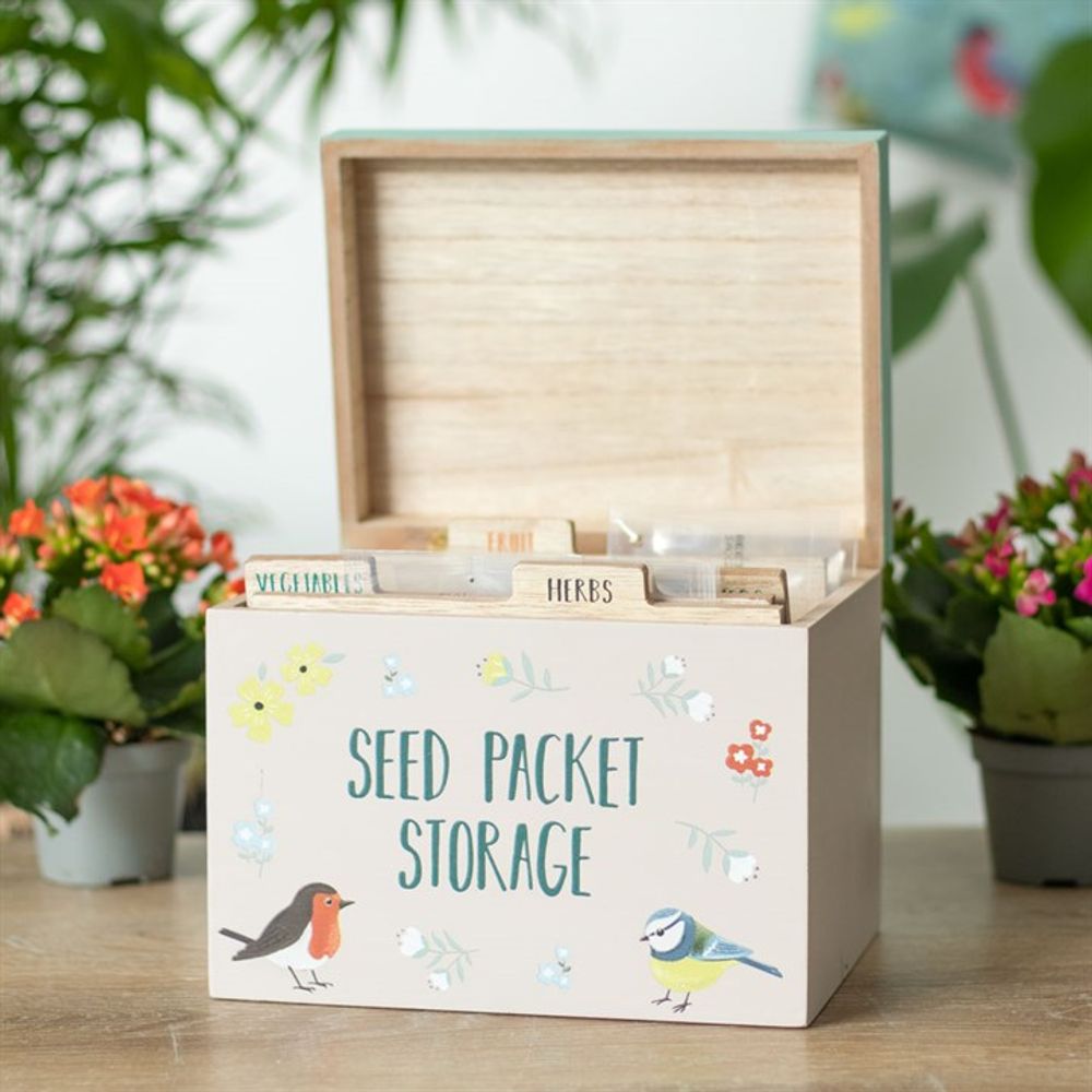 The British Garden Birds Seed Packet Storage Box, illustrated with a robin and blue tit, makes an ideal gift for gardeners. It opens to dividers for herbs, vegetables, and seeds, all beautifully displayed on a wooden table with potted plants in the background.