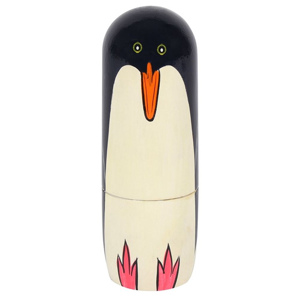 A small, cylindrical wooden figure named "Penguin Russian Doll," carefully hand-painted to resemble a penguin with a black head and back, a white front, yellow eyes, an orange beak, and pink feet. Its top and bottom halves are separated by a visible horizontal seam, making it the perfect home ornament.
