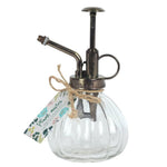 The Botanical Plant Mister showcases a vintage-style glass design with charming ribbed details and a sturdy metal nozzle. Ideal for your indoor garden, it features a rustic metal pump and comes with a decorative tag adorned in floral patterns, labeled "Plant Mister." Its classic look enhances any space with added charm.