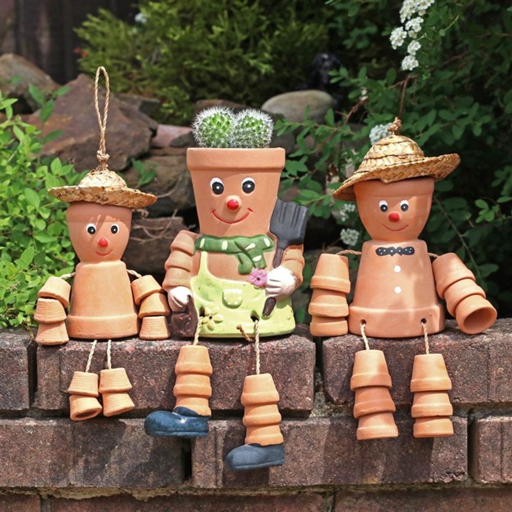 On a brick ledge, three Terracotta Pot Man Planters add charm to your garden with painted faces and straw hats. The centerpiece sports a living botanical hairstyle as a plant grows from its head, surrounded by lush greenery.