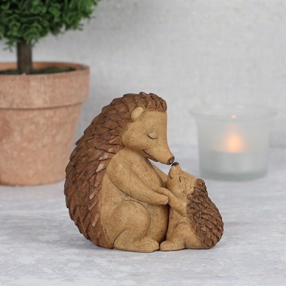 The Happy Hoglet Mother and Baby Hedgehog Ornament captures a gentle moment between a mother and baby hedgehog. A potted plant and lit candle in the background add softness, making it an ideal gift for nature lovers.