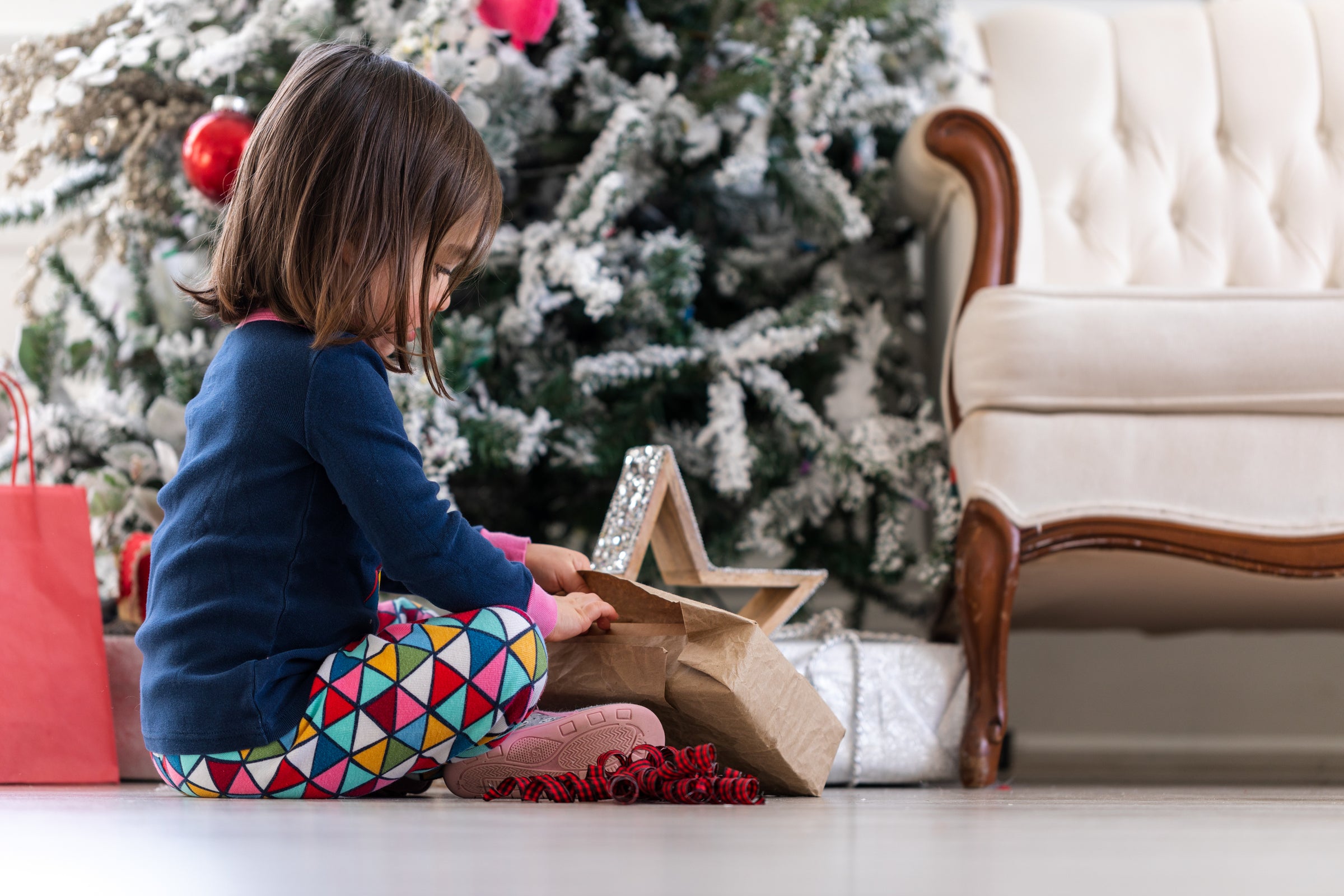 A small child opening a present in front of a christmas tree.