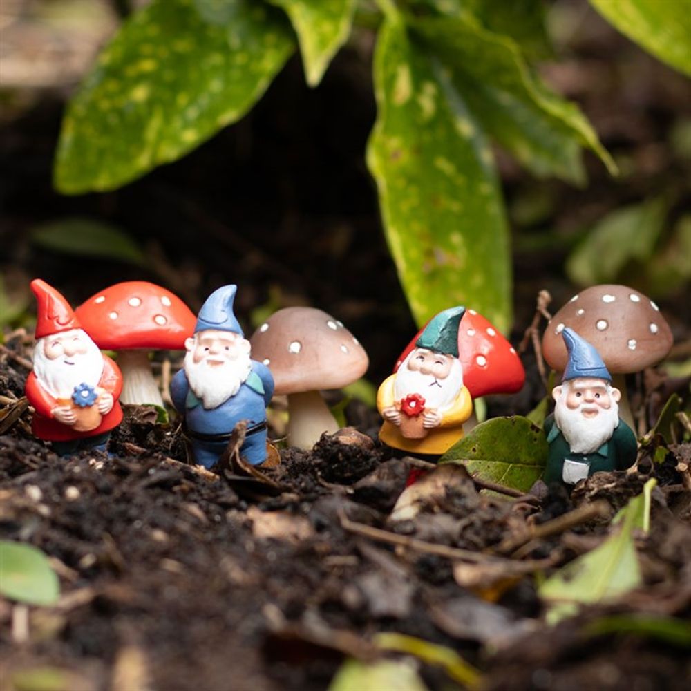 The Set of 4 Mini Gnome Plant Pot Pals stand amidst vibrant red and brown spotted mushrooms, creating a whimsical fairy garden surrounded by lush green foliage.