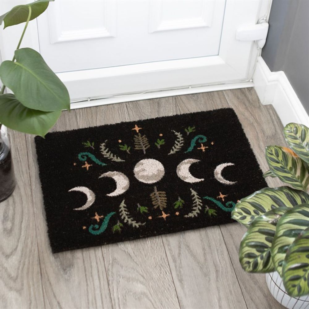 The entry near the white door is adorned with the Black Dark Forest Moon Phase Doormat, featuring a captivating moon phase design. Green and brown botanical illustrations surround the moons, creating a magical effect that complements the nearby potted plants and adds charm to the light wooden floor.