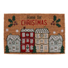 The Natural Home For Christmas Doormat is a festive addition featuring the text "Home for Christmas" at the top. It showcases a charming design of five red and white houses adorned with wintery decorations, all set in a Christmas village scene. The doormat is bordered by holly leaves and berries, as well as small snowflakes, against its natural coir texture background.