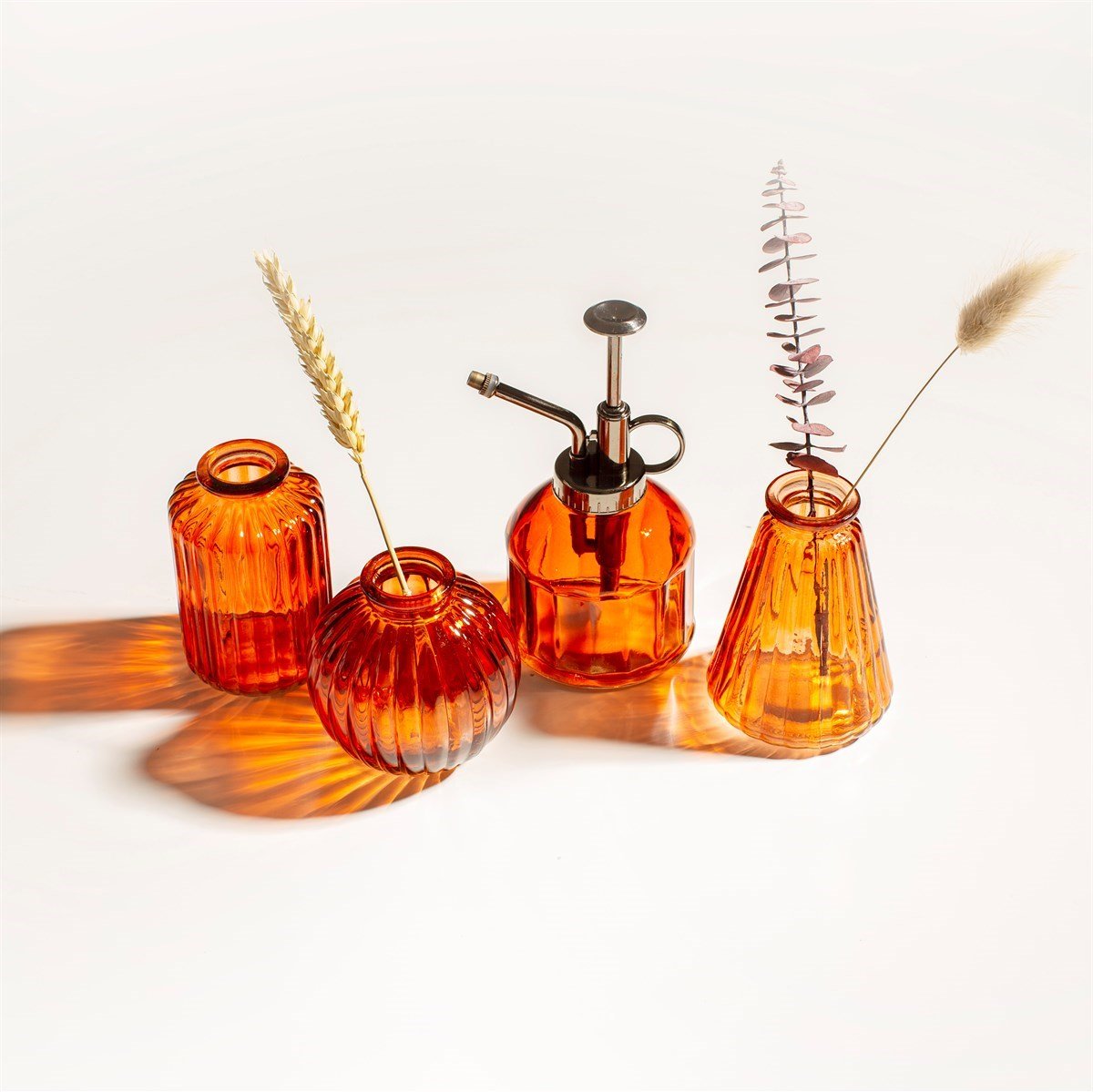 A range of orange/red plant misters and spray bottles made of glass