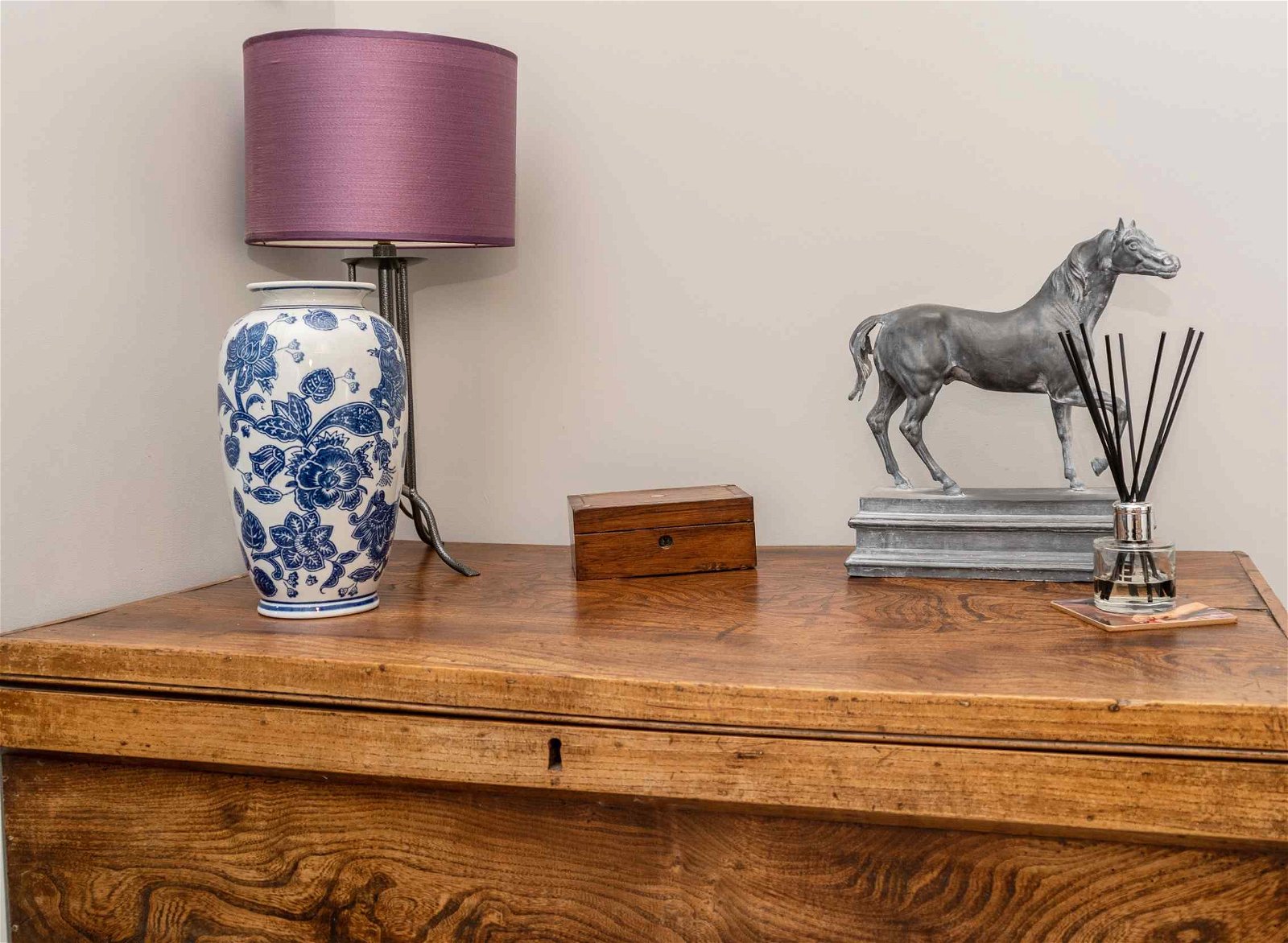 A tall floral vase shown with a lamp on a wooden table.