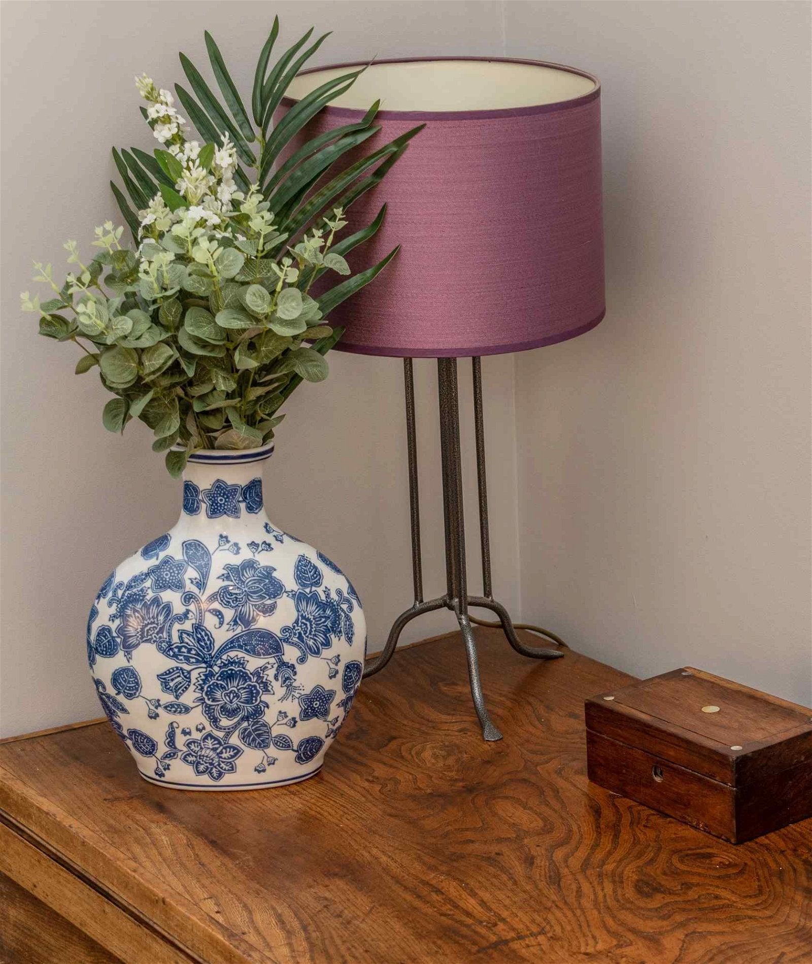 A floral vase shown with a lamp and plants on a table.