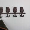 The Rustic Cast Iron Wall Hooks, Owls offers an industrial style charm with its four owl-shaped metal hooks. Ideal for small space storage, it features a jacket hanging on the leftmost hook, while a green plant on the right adds to the scene against a light-colored wall.