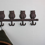 The Rustic Cast Iron Wall Hooks, Owls offers an industrial style charm with its four owl-shaped metal hooks. Ideal for small space storage, it features a jacket hanging on the leftmost hook, while a green plant on the right adds to the scene against a light-colored wall.