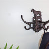 A coat hangs on a vintage-inspired Cast Iron Wall Mounted Rotating Coat Hooks with a horse design. Green plant leaves peek from the bottom left against a light wall, enhancing the industrial charm.