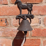 The Rustic Cast Iron Wall Bell, Horse, features a charming horse figure and hangs from a red brick wall with a short white rope—a perfect accent for farmhouse decor and horse enthusiasts.