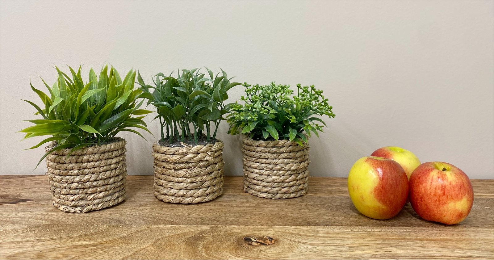 Three pots made of rope shown with green artificial succulents inside on a wooden table with candles