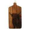 The Highland Cow Engraved Wooden Cheese Board is a rectangular mango wood cutting board with a handle, showcasing an intricately engraved portrait of a Highland cow with long horns and shaggy fur. The board can be conveniently hung by the loop of twine attached to the handle.