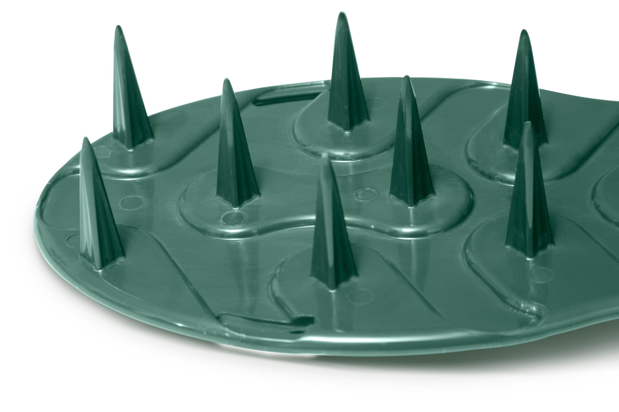 A close-up view of the ProSpike Lawn Aerator Shoes with Plastic Straps reveals a green plastic surface featuring multiple cross-shaped spikes arranged in rows. The slightly curved, glossy finish of the object makes it reminiscent of a lawn aerator shoe.