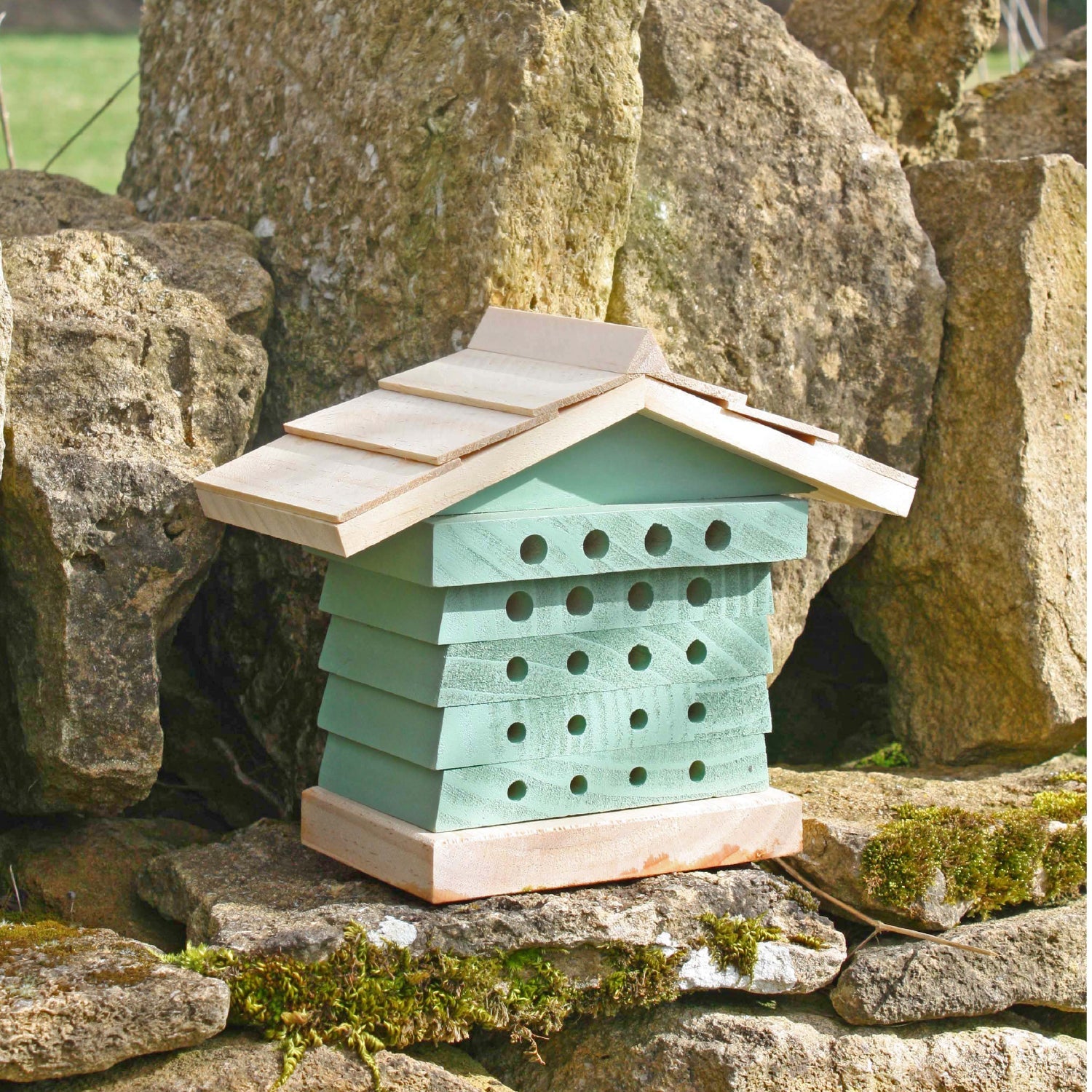 A wooden bee house in natural wood and painted sea green shown on a traditional stone wall.